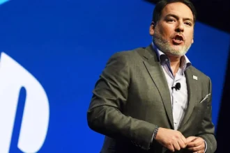 Ο Shawn Layden μπροστά από το λογότυπο του PlayStation με φόντο δημοφιλή αποκλειστικά παιχνίδια