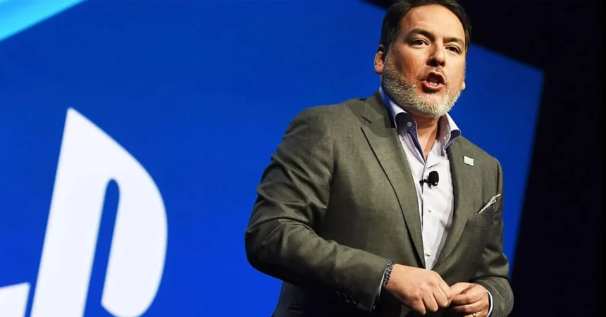 Ο Shawn Layden μπροστά από το λογότυπο του PlayStation με φόντο δημοφιλή αποκλειστικά παιχνίδια