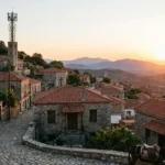 Μια κεραία 5G να δεσπόζει διακριτικά πάνω από ένα παραδοσιακό ελληνικό ορεινό χωριό με πέτρινα σπίτια