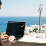 Developer πληκτρολογεί σε laptop με φόντο το Αιγαίο σε νησί με 5G κάλυψη